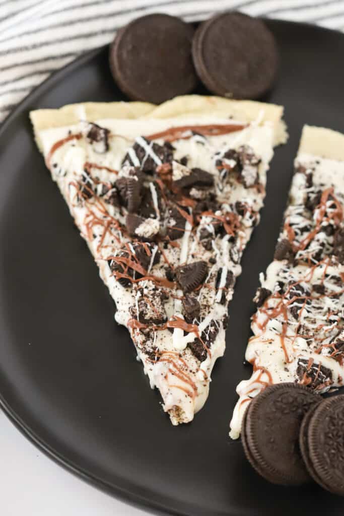 A serving plate with two slices of Oreo Dessert Pizza drizzled with white chocolate and caramel sauce. Oreo desserts, oreo dessert ideas, oreo pizza.
