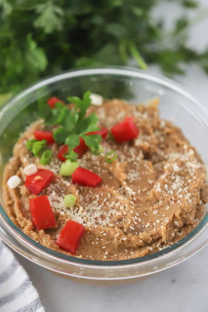 A serving bowl full of Refried Beans topped with sliced peppers and onions. Mexican refried beans recipe. Refried beans recipe authentic, black refried beans recipe.