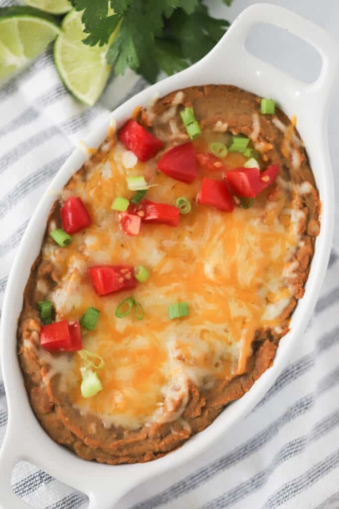 A cast iron dish full of Refried Beans topped with melted cheese. Authentic Mexican refried beans recipe. Refried beans recipe authentic, refried beans recipe crock pot.