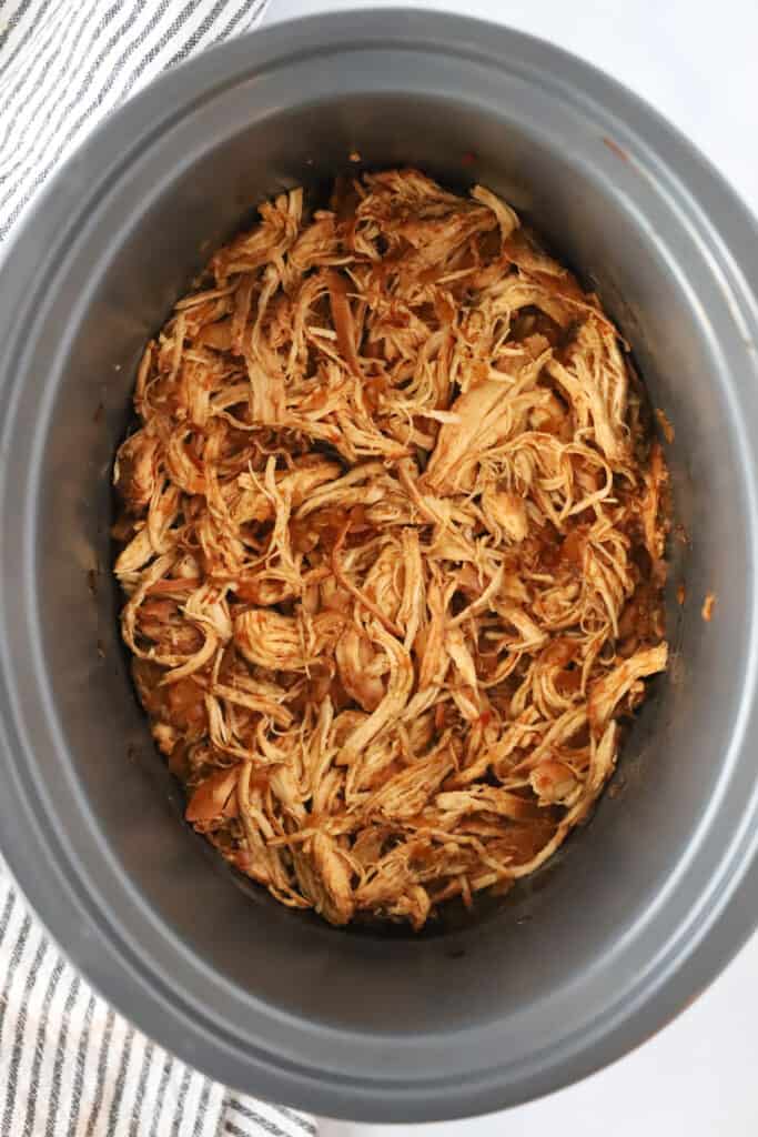 A crockpot full of Slow Cooker BBQ Chicken. slow cooker shredded bbq chicken, bbq chicken sliders slow cooker. 