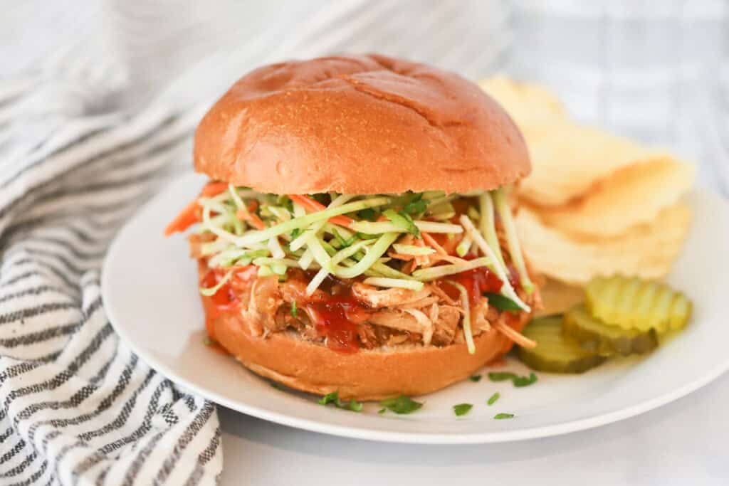 A dinner plate with a Tangy Crockpot Chicken Sliders, pickles, and potato chips.