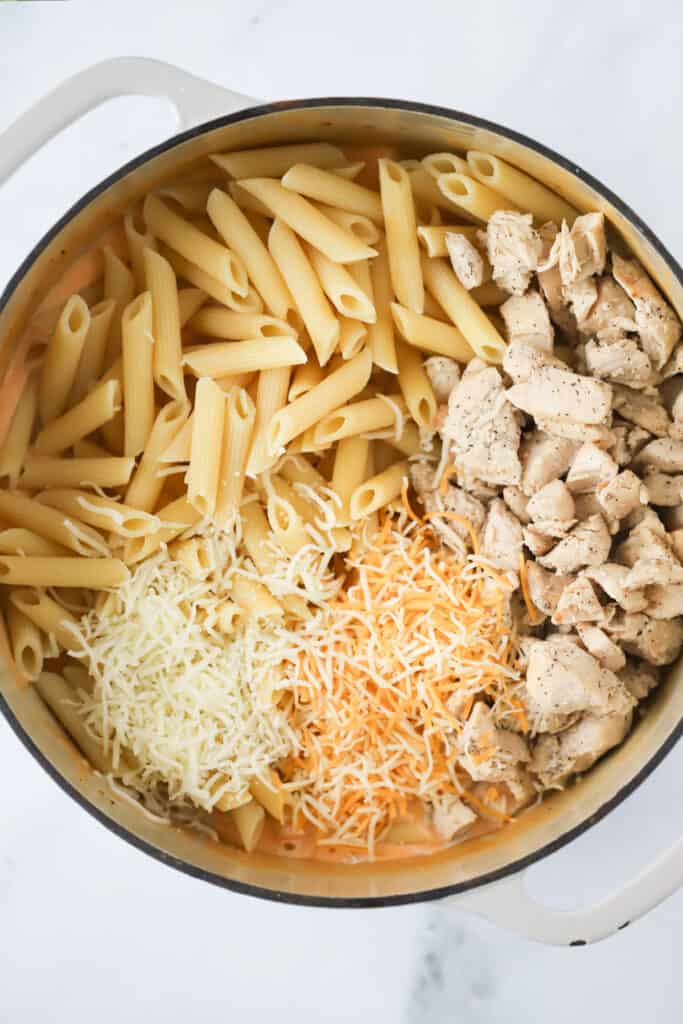 A dutch oven with cooked pasta, cooked chicken, and shredded cheese ready to mix together. Buffalo ranch chicken pasta, shredded chicken pasta, buffalo chicken alfredo.