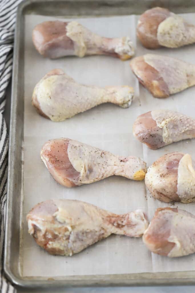 A sheet tray lined with parchment paper and chicken drumsticks ready to bake.