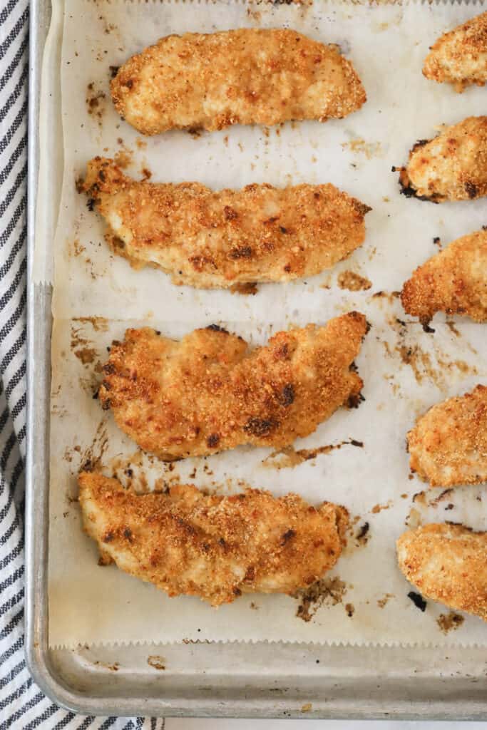 A sheet tray full of oven-baked Chicken Tenders. Oven fried chicken tenders, how to cook chicken tenders in the oven, oven baked chicken tenderloins, baked chicken strips recipe, baked chicken tenders recipes.