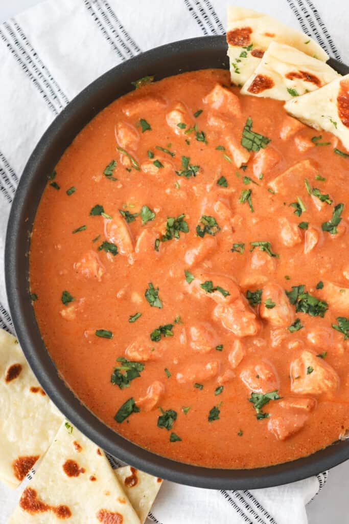 A bowl full of Chicken Tikka Masala topped with fresh cilantro and a side of Naan bread. chicken tikka recipe. tiki masala. 