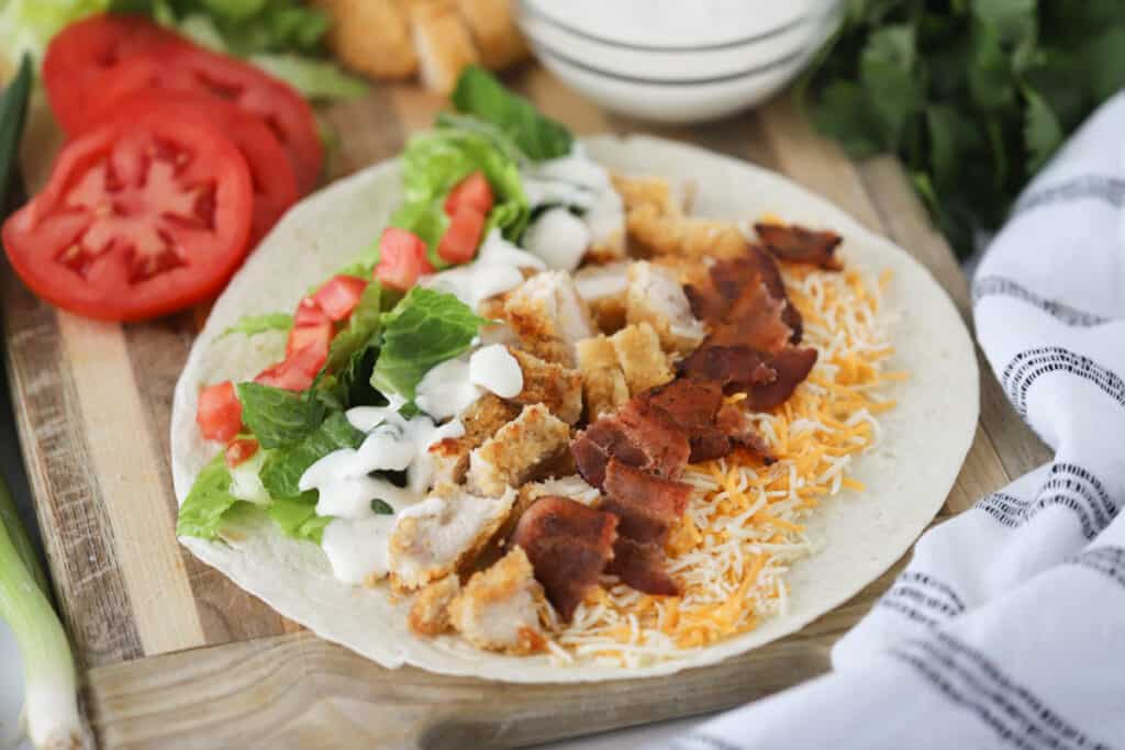 A large flour tortilla filled with ingredients to make a chicken and bacon wrap.