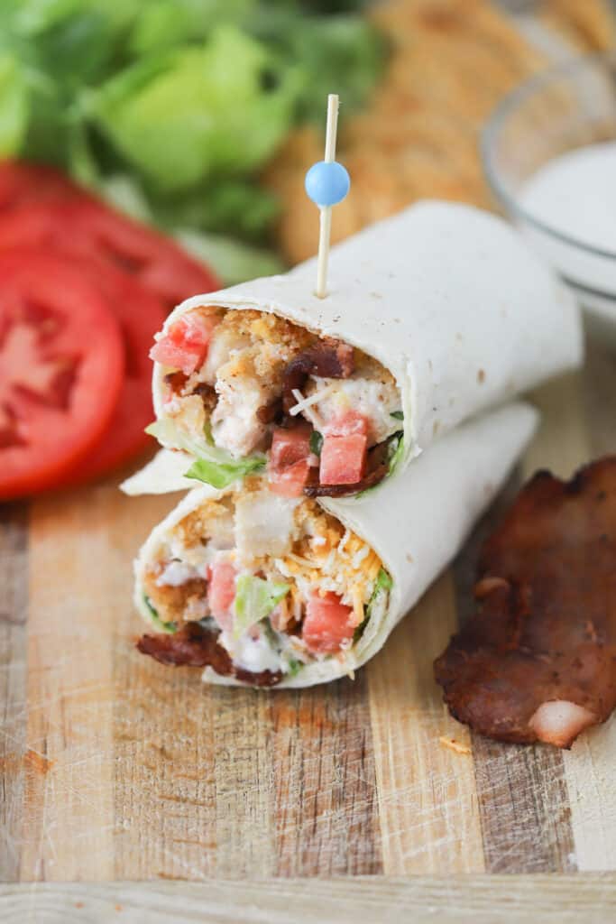 A Chicken and Bacon Wrap cut in half on a cutting board. Chicken bacon wrap recipes. Crispy chicken ranch wrap. Crispy chicken wrap.