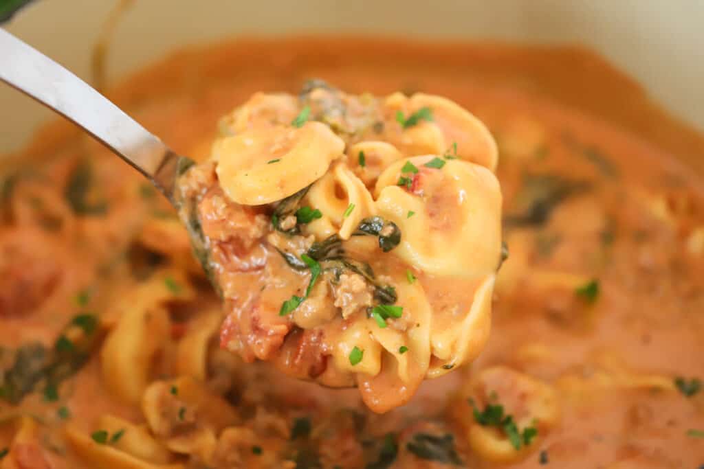 A ladle full of soup with tortellini and sausage, tortellini creamy soup. 
