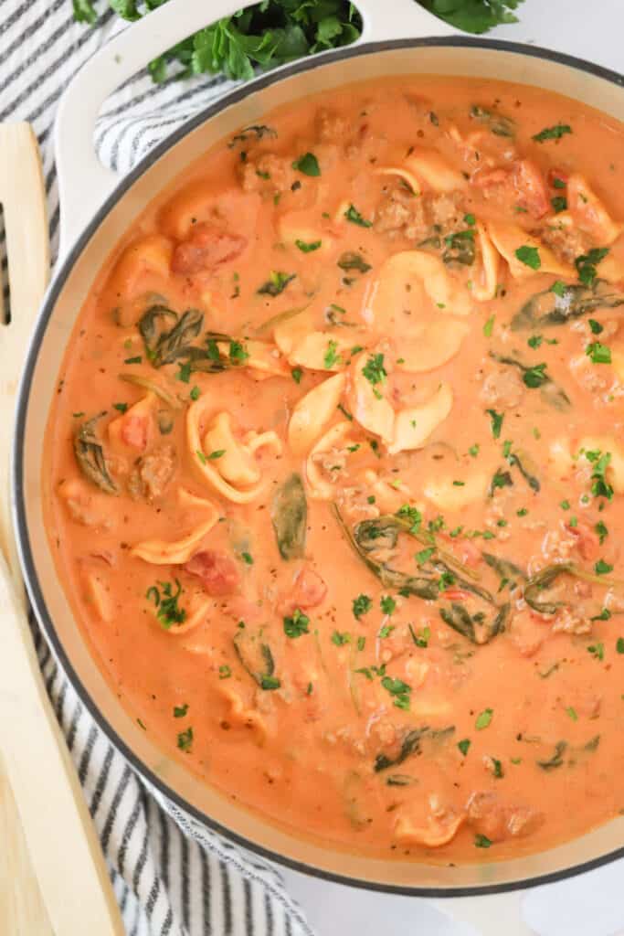 A Dutch oven full of creamy tortellini soup with spinach.