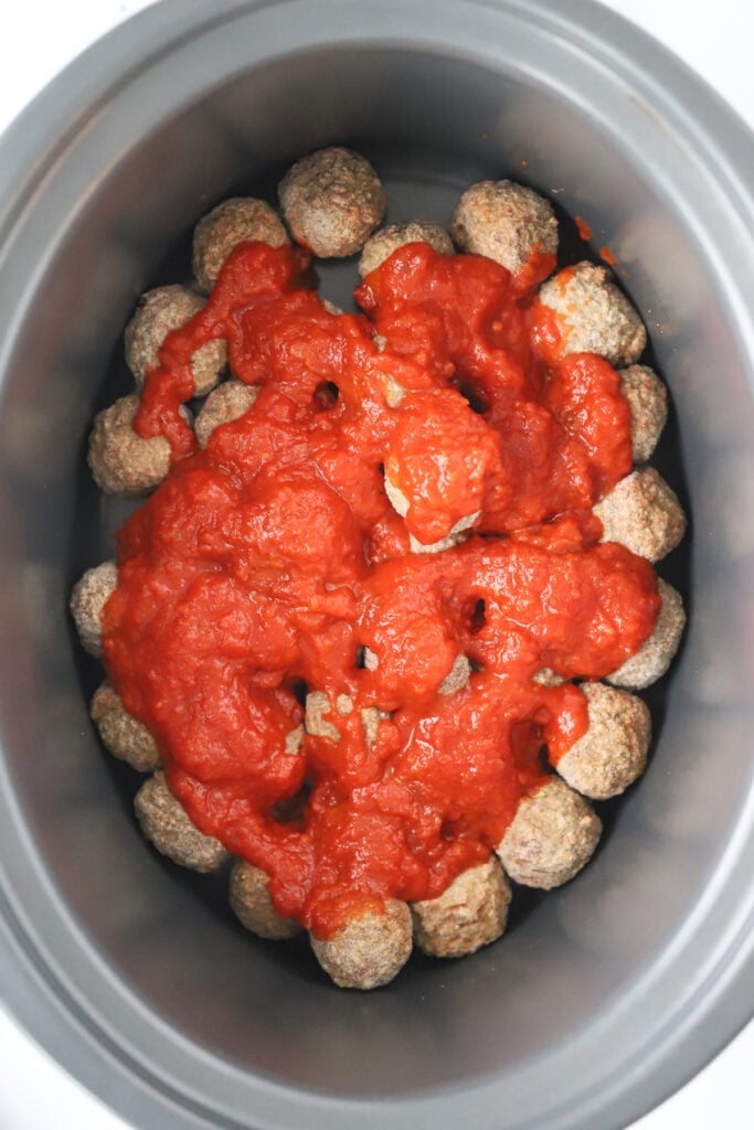 A crockpot full of frozen meatballs topped with marinara sauce; frozen meatballs crockpot.