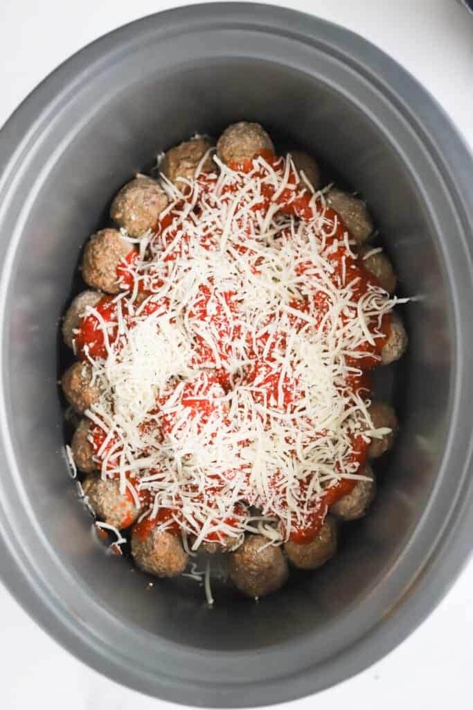 a crockpot full of frozen meatballs topped with marinara sauce and shredded cheese; frozen meatballs in crockpot. Slow cooker italian meatballs.