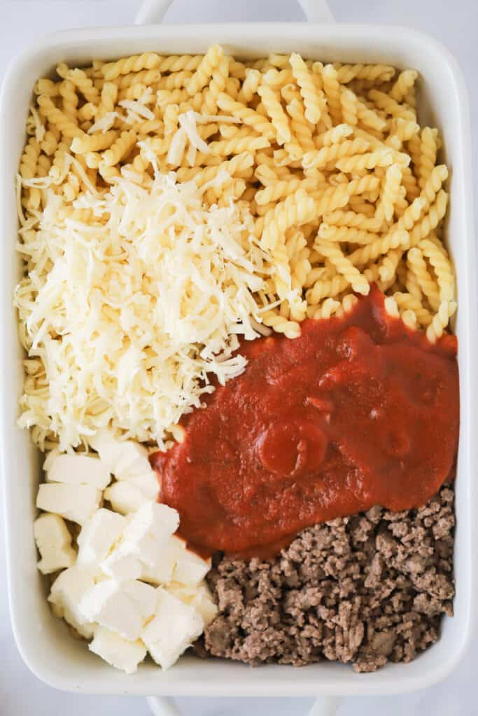 A baking dish with the ingredients to make a cheesy beef pasta dish. penne pasta bake with ground beef. Baked beef pasta. Pasta ground beef recipe.