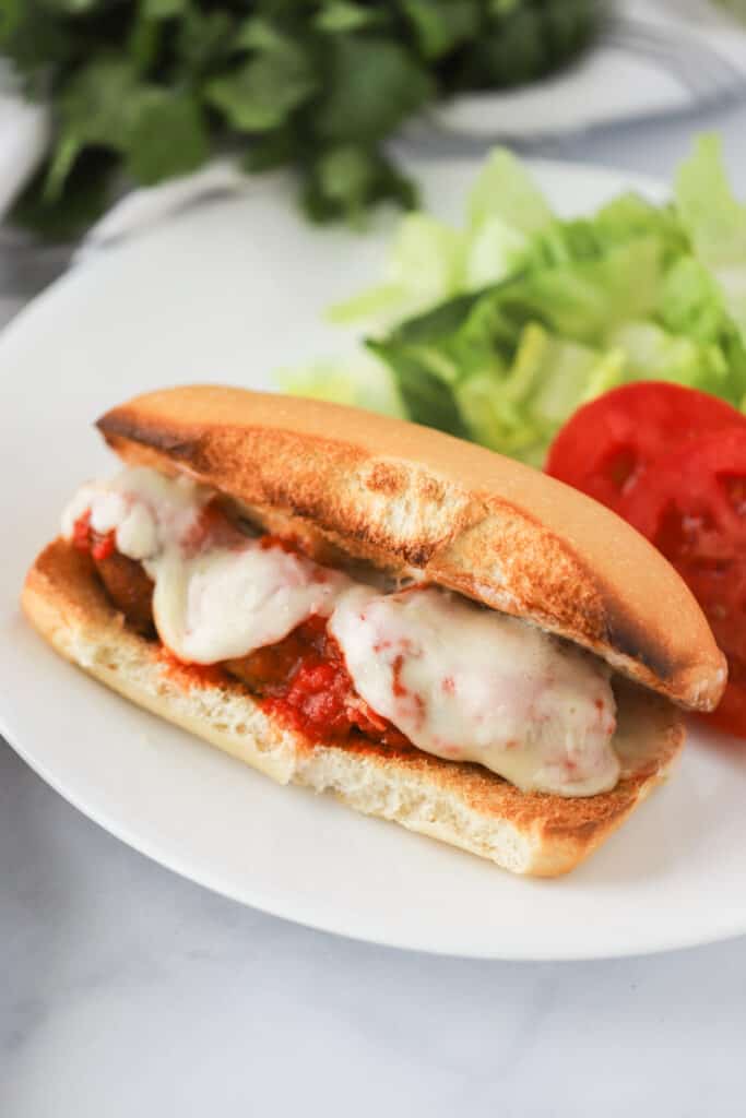 A dinner plate with a Meatball Sub Sandwich topped with melted cheese and marinara sauce; best meatball sandwich near me; meatball sub recipe.