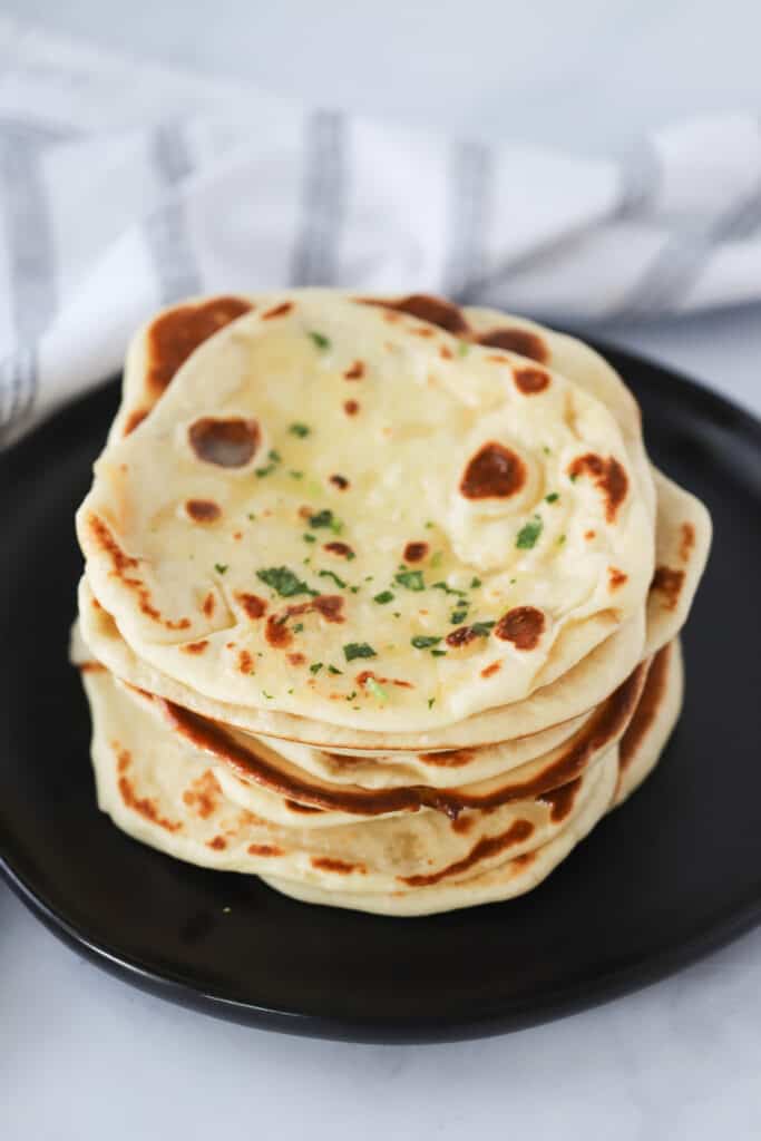 A stack of Naan bread on a black plate. Homemade Naan bread recipe with yogurt, naan bread recipes, recipes for naan bread.