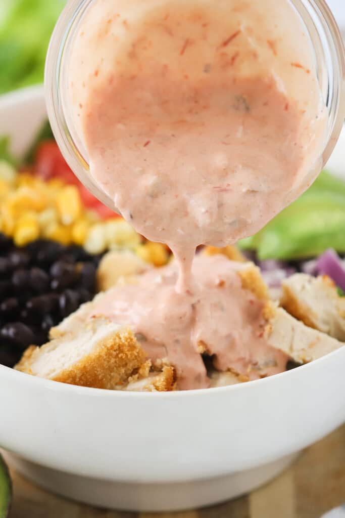 Dressing being poured over crispy Southwest salad chicken. Southwest chicken bowl, crispy chicken salad recipes. southwest salad recipe chicken, salad with crispy chicken.