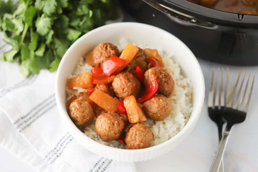 Sweet and sour meatballs crockpot recipe with red peppers and pineapples in a bowl over white rice.