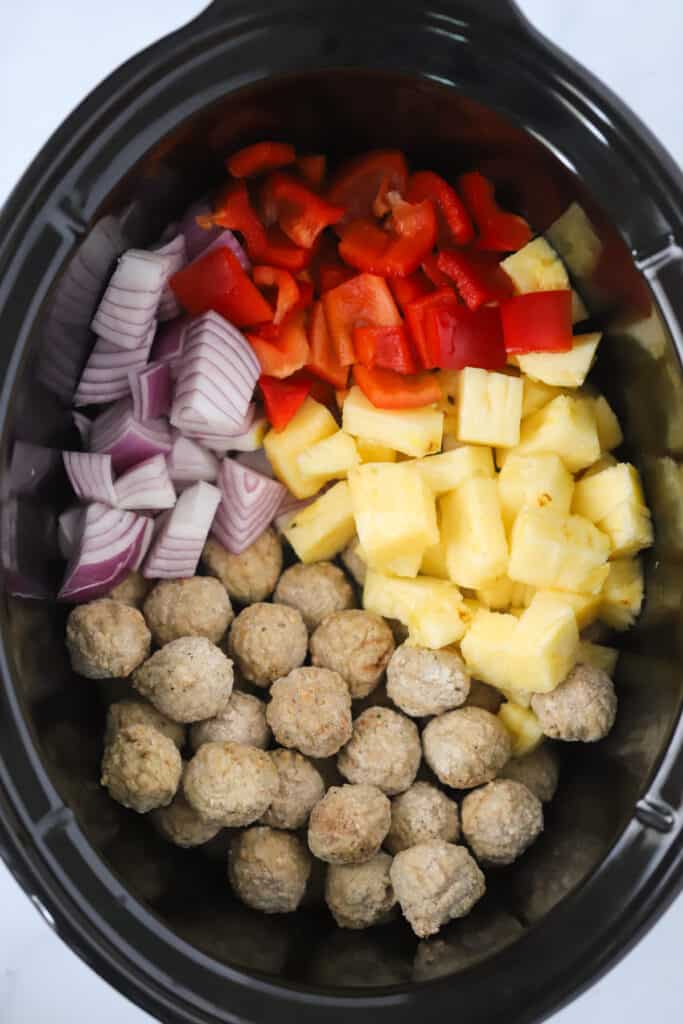 Ingredients for sweet and sour meatballs in crockpot including onions, pineapples, and red peppers.