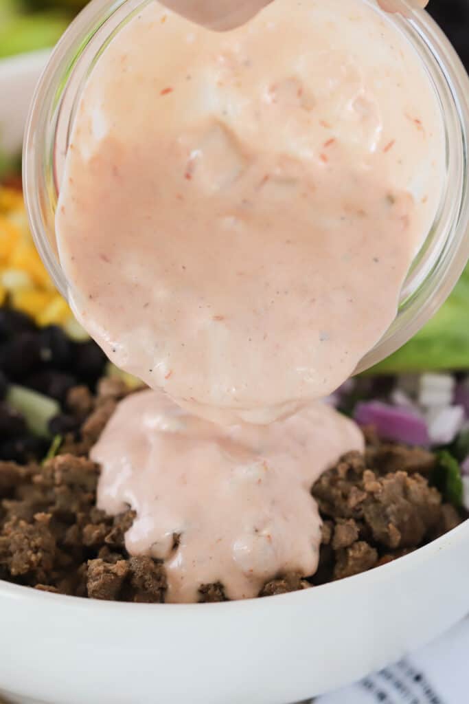 Taco Salad Dressing being poured over the ingredients in a bowl. Easy taco salads.
