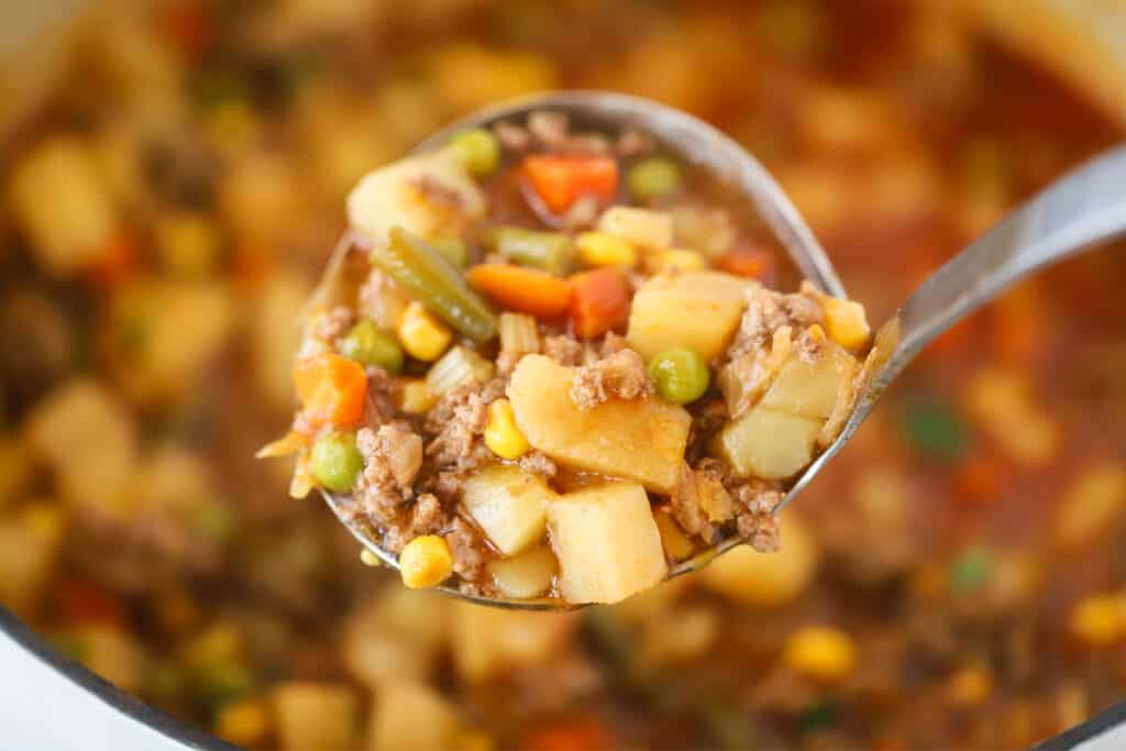 A ladle full of soup with beef, potatoes, and vegetables. ground beef vegetable beef soup recipe. 