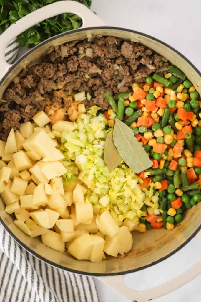 A dutch oven full of ingredients for making Vegetable Beef Soup. vegetable ground beef soup, vegetable beef soup with ground beef. 