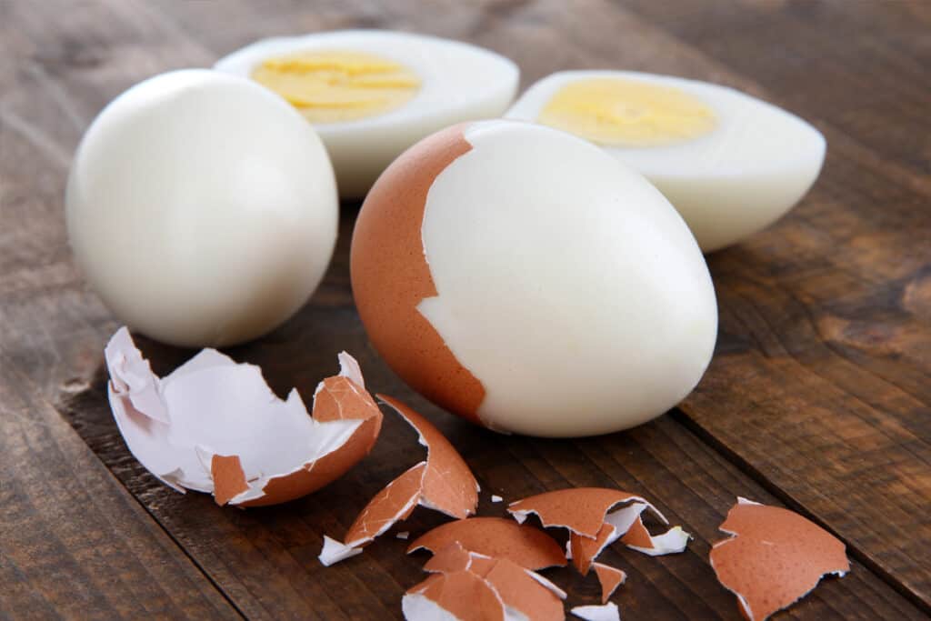 Hard Boiled Eggs on a tabletop with shells being removed; making hard boiled eggs with baking soda.