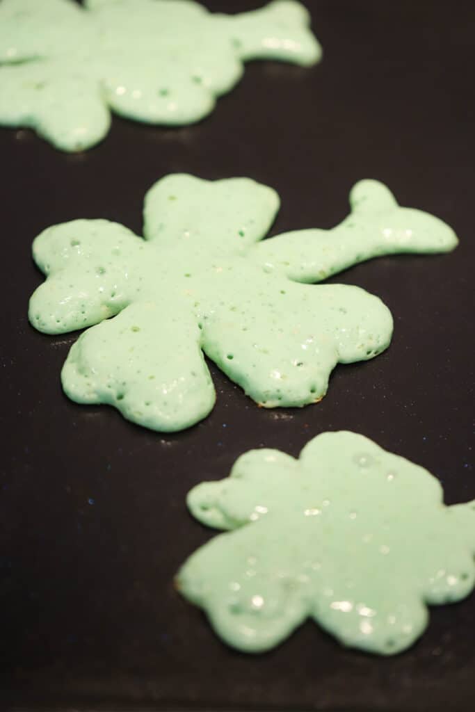Green Shamrock Pancakes cooking on a griddle.