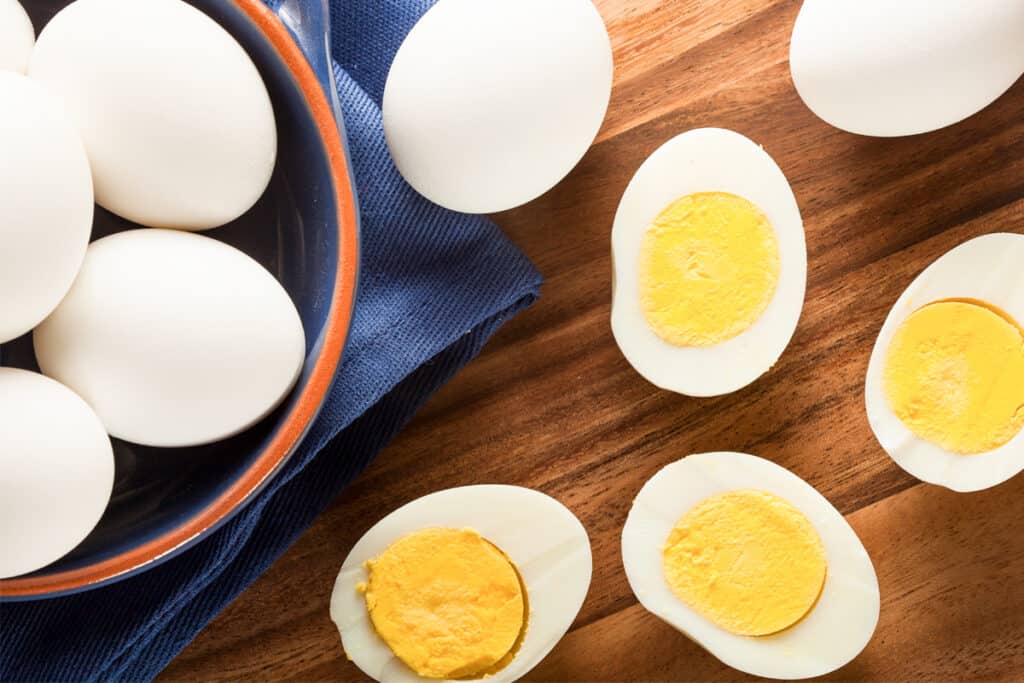 A bowl of hard boiled eggs next to cooked eggs cut in half; boiled eggs baking soda.