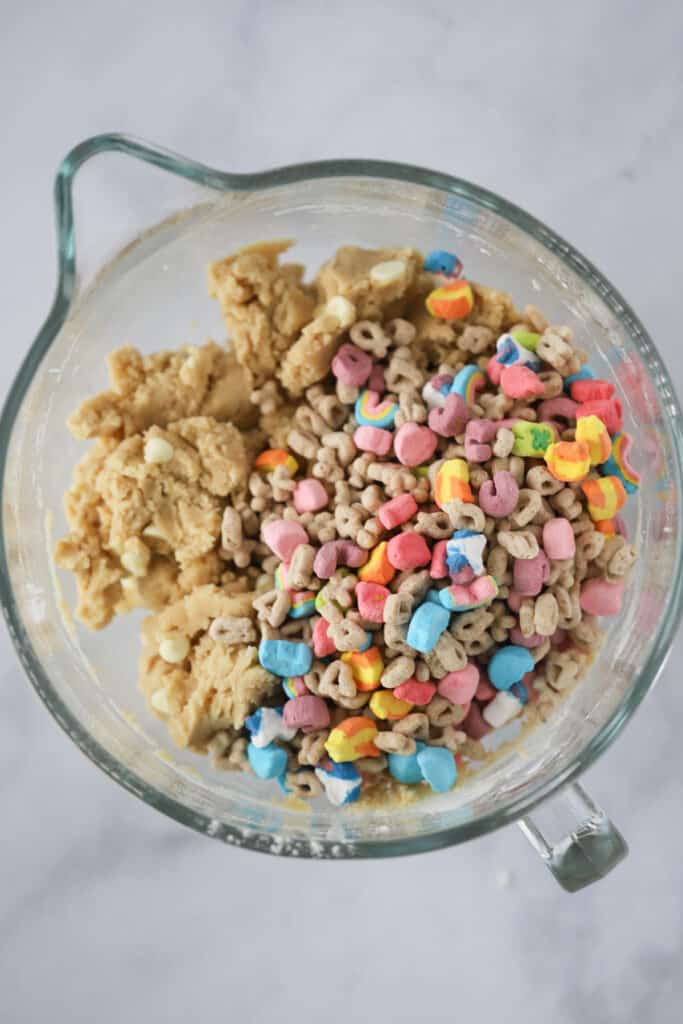 A glass measuring cup full of Lucky Charms cereal and cookie dough.