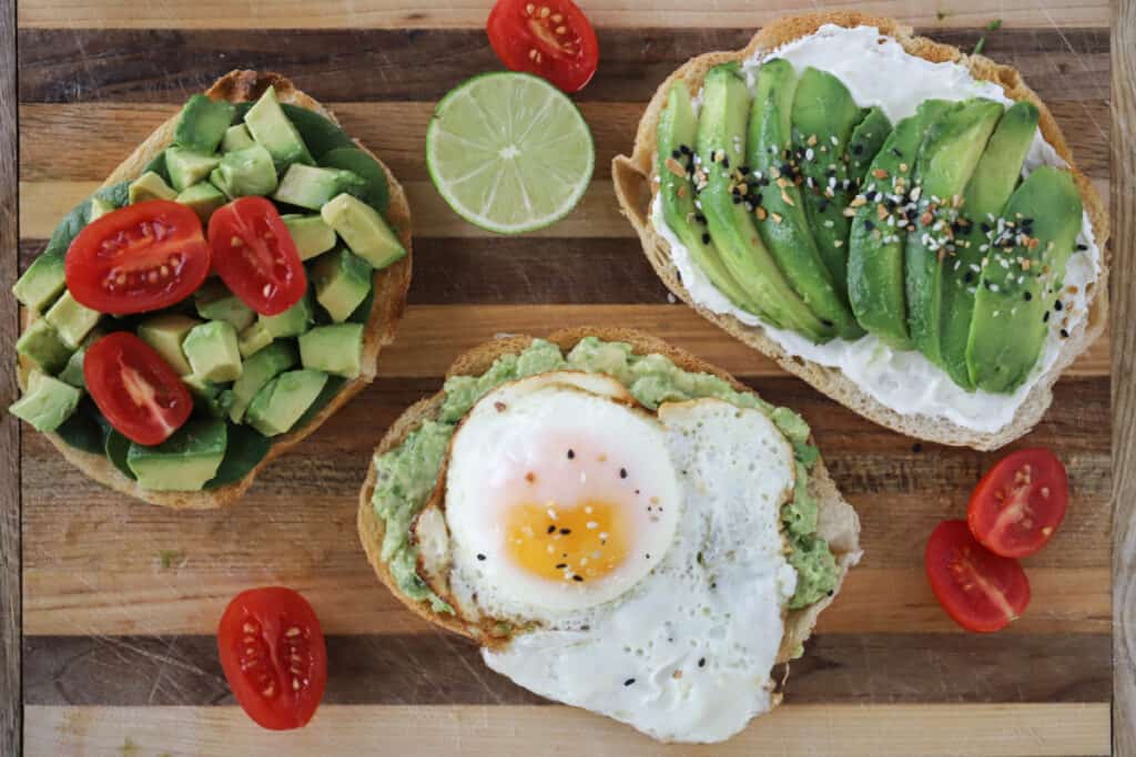 A cutting board with variations Avocado Toast flavor variations including avocado toast with eggs. Cream cheese avocado toast.