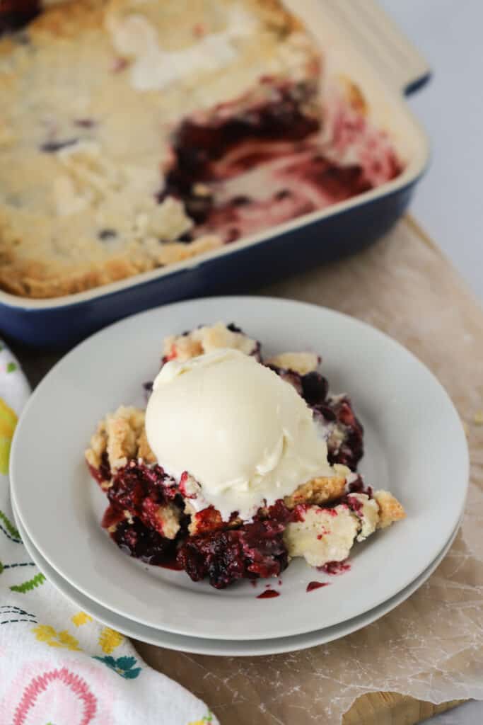 A plate with triple berry cobbler topped with a scoop of vanilla ice cream. Best berry cobbler with cake mix. Easy berry cobbler recipe.