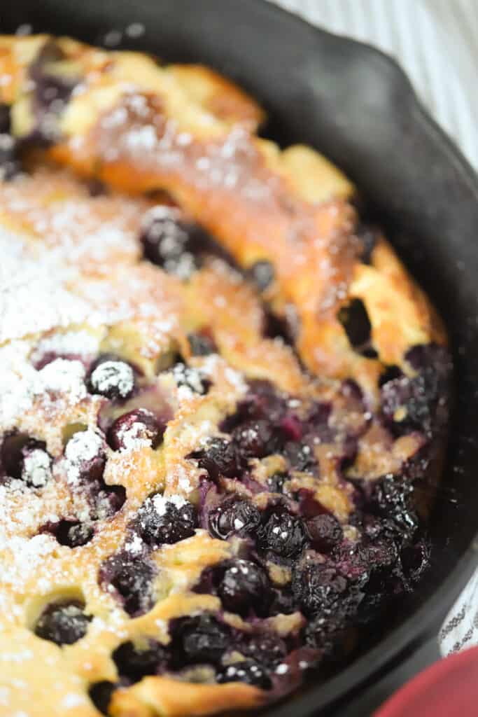 A skillet with a lemon blueberry dutch baby topped with powdered sugar. Dutch baby pancakes recipe. Blueberry german pancake recipe.