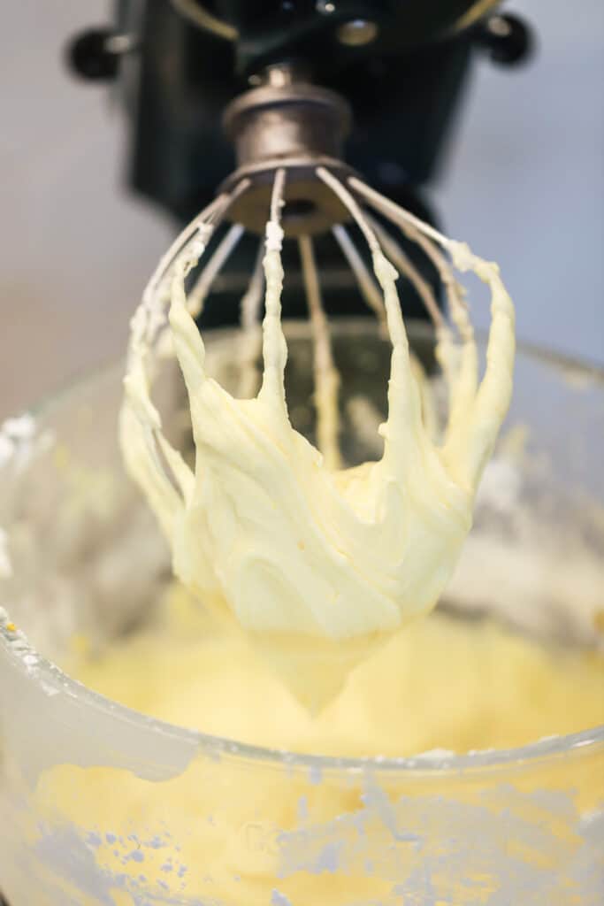 A stand mixer with a whisk making cream cheese lemon frosting, cream cheese frosting lemon, lemon icing cream cheese, lemon cream cheese dessert, lemon dessert with cream cheese.