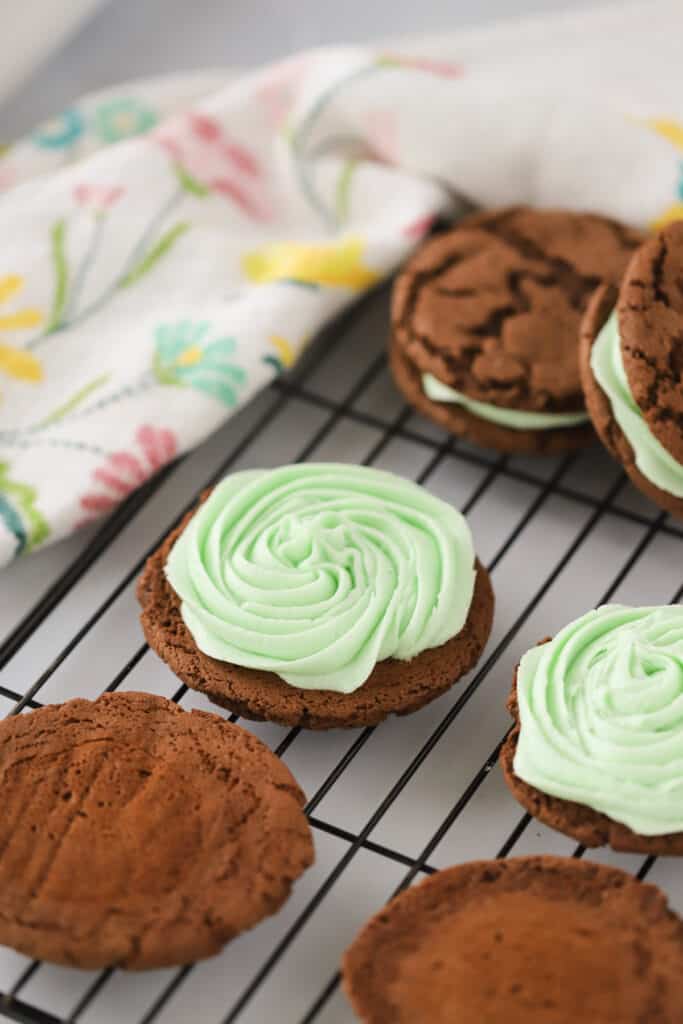 Chocolate cookie sandwiches filled with Mint Cream Cheese Frosting on a wire rack. Buttercream mint frosting. Mint Icing.