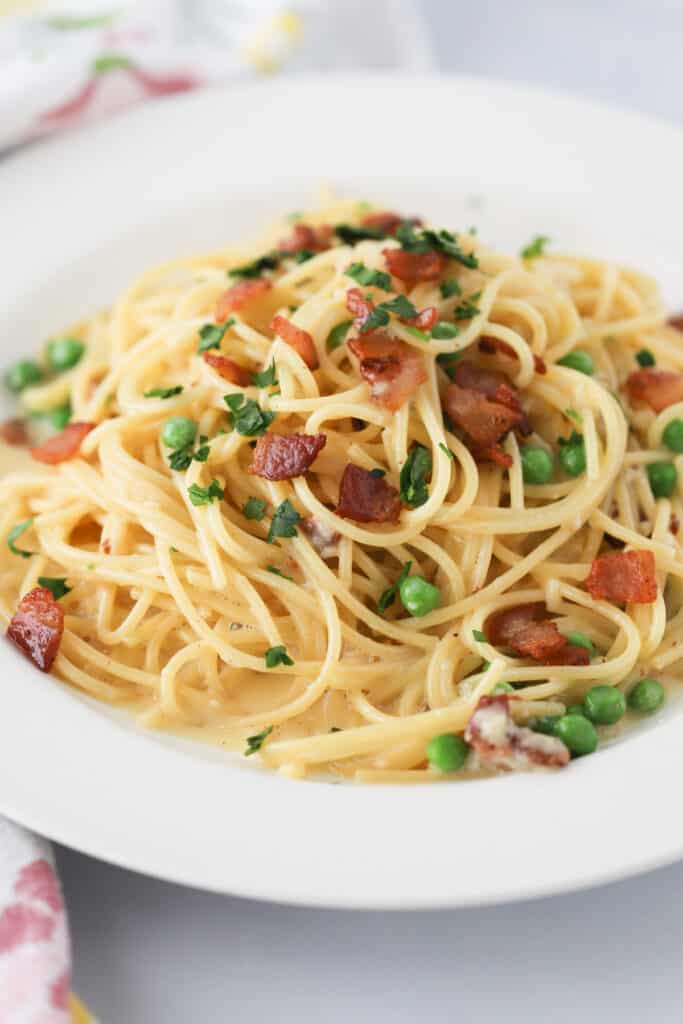 A plate full of Spaghetti Carbonara topped with bacon and peas.