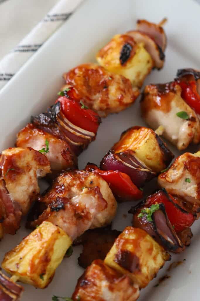 chicken bacon pineapple kabobs on a white plate; chicken kabobs with pineapple; how to grill chicken kabobs, bacon pineapple chicken kabobs, pineapple bacon chicken kabobs.