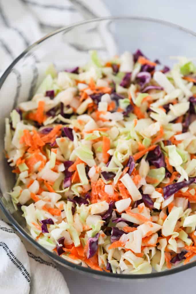 A glass mixing bowl full of our traditional coleslaw recipe with mayonnaise, shredded cabbage, carrots, and the best coleslaw dressing recipe.