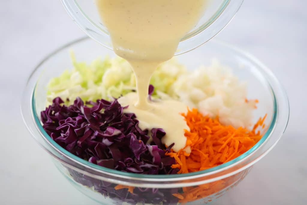 Creamy coleslaw dressing being poured over shredded cabbage and carrots. Whats in coleslaw.