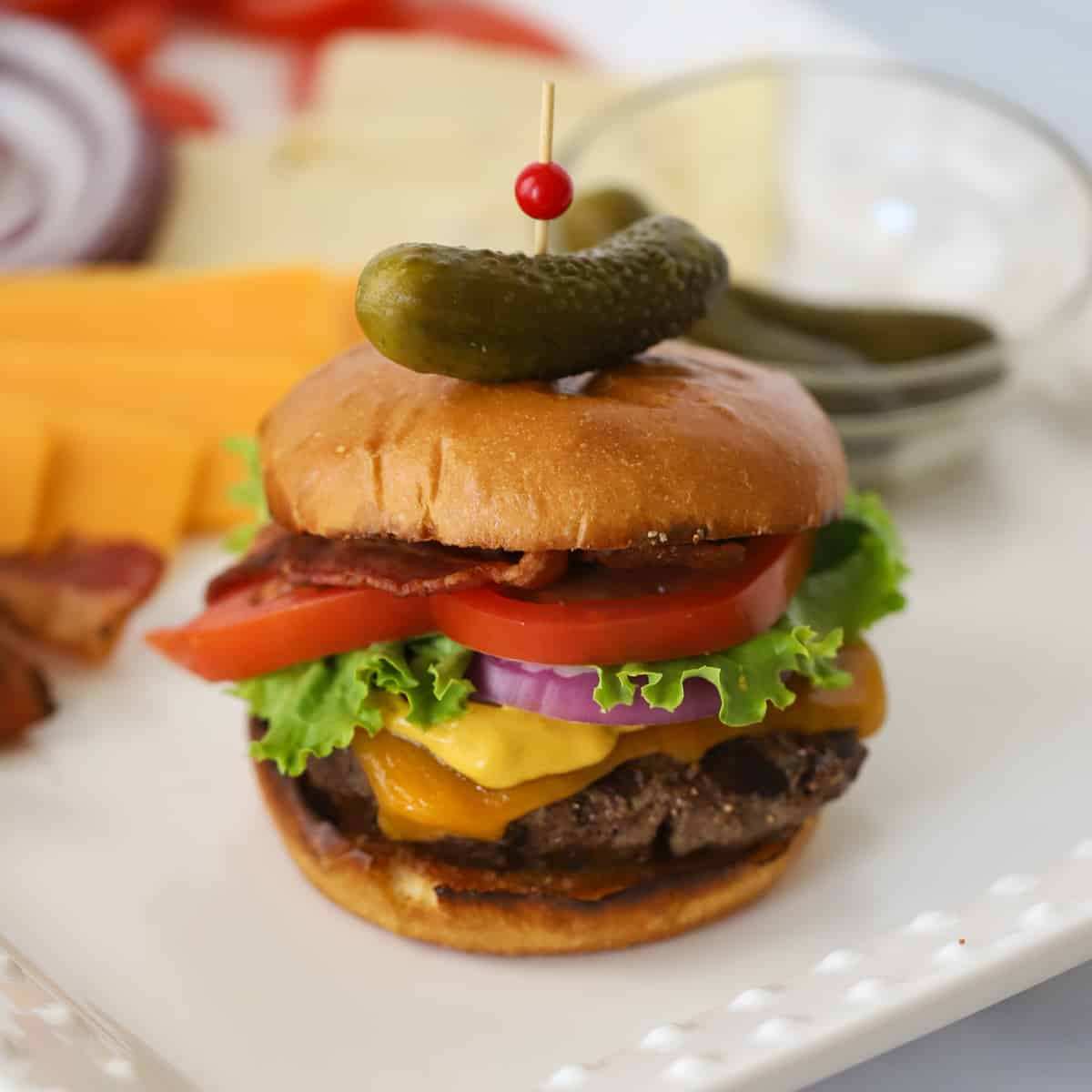 A hamburger on a plate with a mini pickle on top.