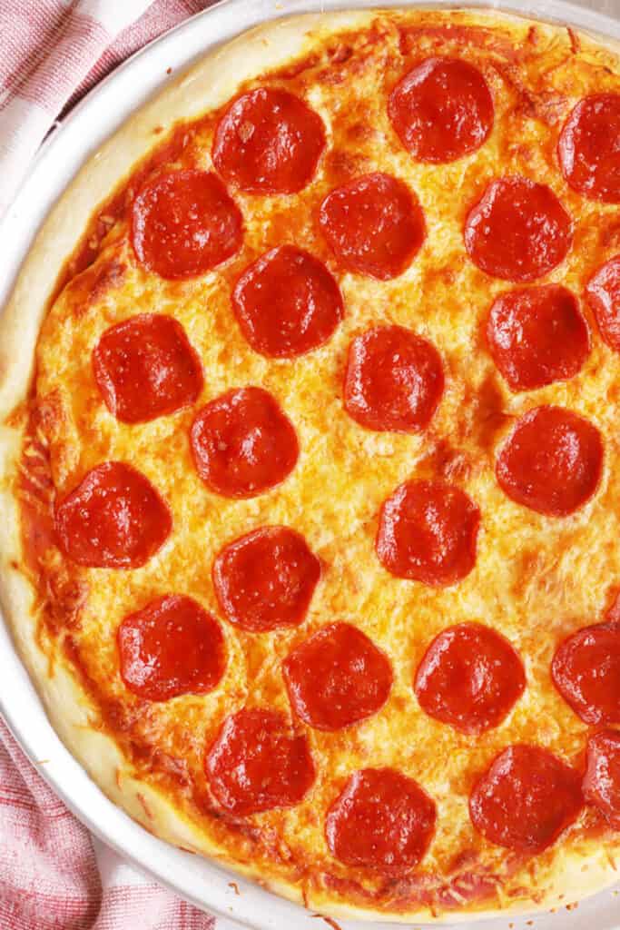 Basic pizza Dough recipe spread onto a pizza pan topped with pizza sauce and cheese. Homemade pizza dough, best homemade pizza recipe.