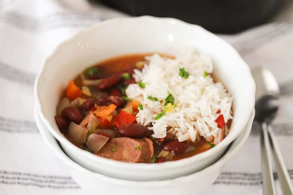 A white serving bowl with Slow cooker beans and rice, a recipe full of sausage, rice, and beans in crock pot.