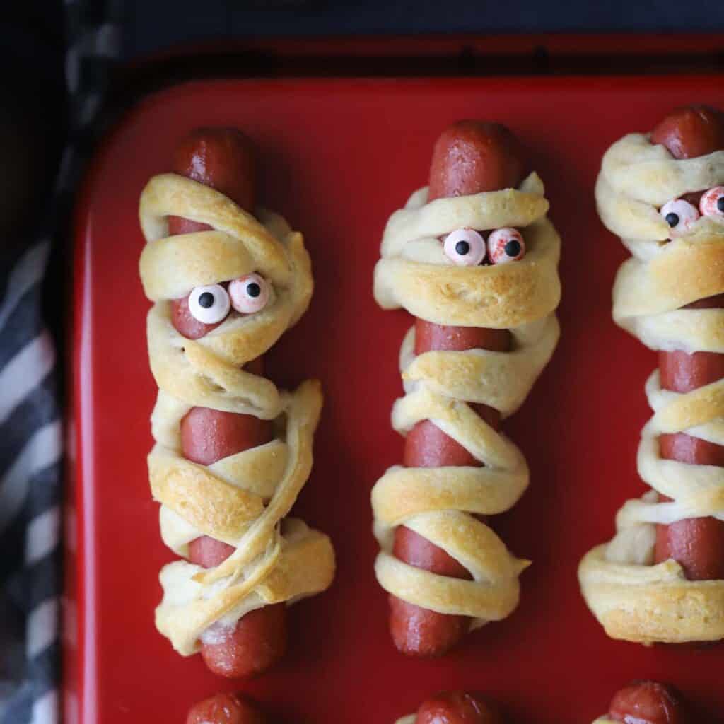 Mummy hot dogs on a red serving tray with candy eyes