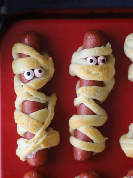 Mummy hot dogs on a red serving tray with candy eyes
