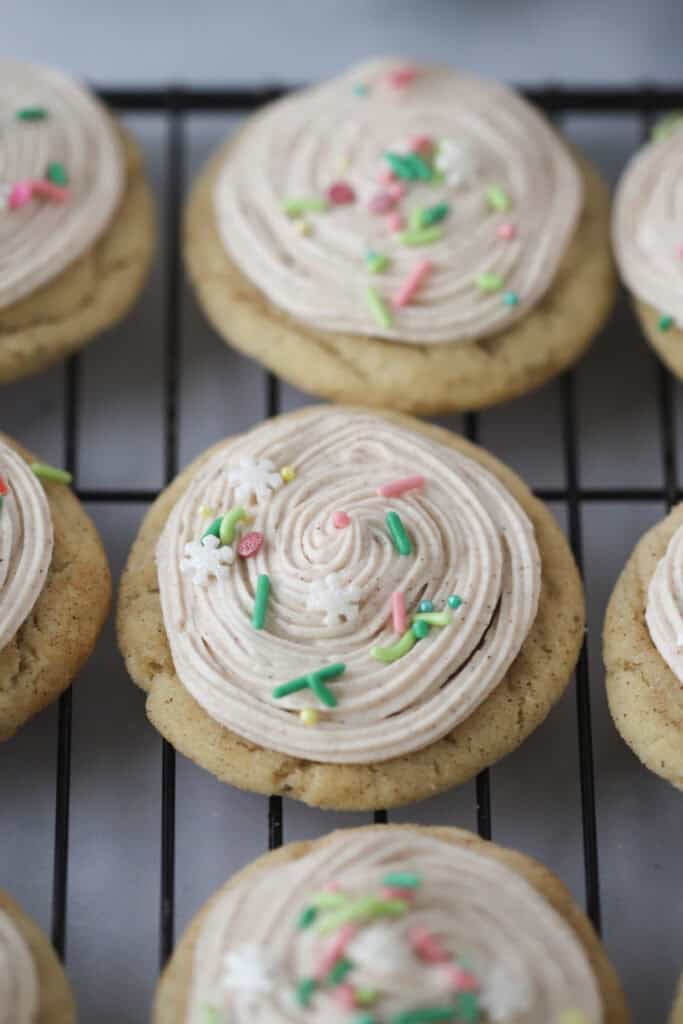 A wire rack with frosted eggnog sugar cookies topped with eggnog buttercream and sprinkles.