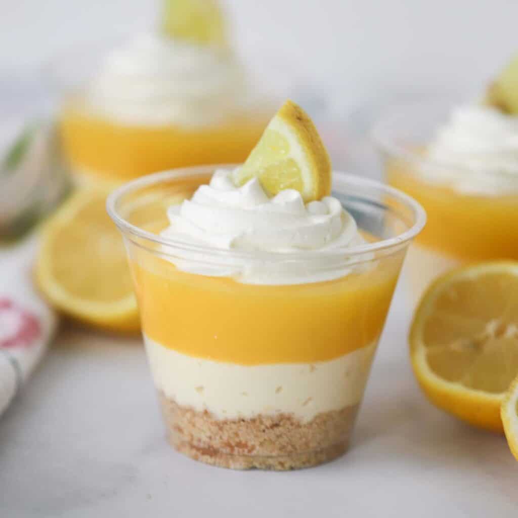 Individual cups with lemon curd parfait dessert topped with whipped cream and fresh lemons.
