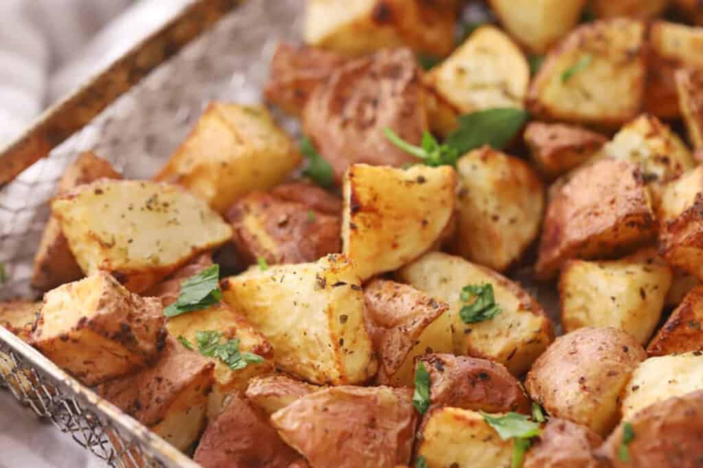 red potatoes in air fryer basket with fried red potatoes topped with fresh chopped parsley.