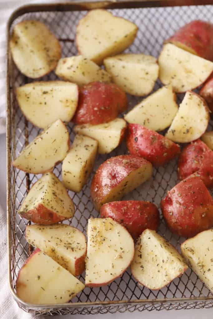 Quartered red potatoes covered in seasoning in an air fryer basket ready to cook. red potatoes air fryer recipe. 