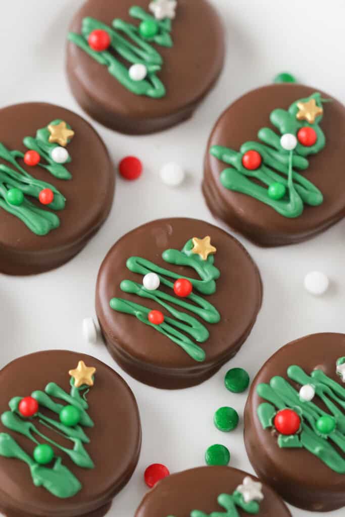 Chocolate covered mint oreos on a baking sheet decorated with little piped trees and festive sprinkles.