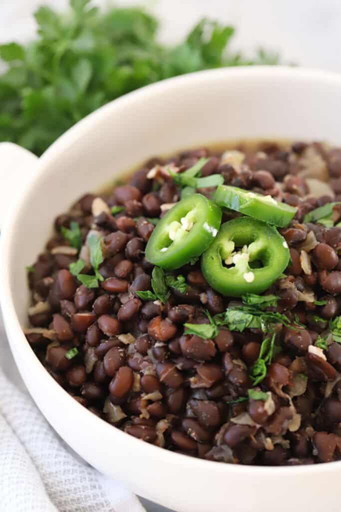 Chipotle Black beans in a serving dish topped with sliced jalapenos and fresh cilantro. black beans chipotle. how to make chipotle black beans, black bean recipe chipotle. 