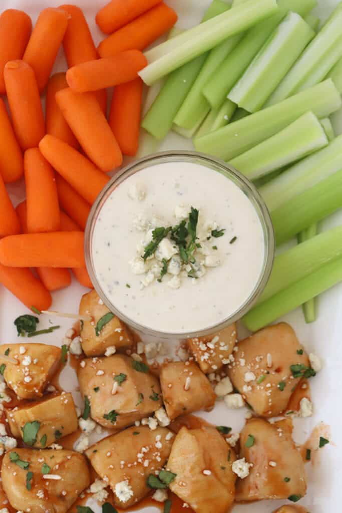 A serving platter with appetizer sized chicken bites baked, a ramekin of dressing, carrots and celery sticks. baked buffalo chicken recipe