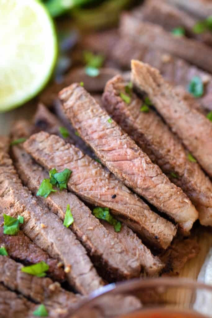 Slices of this authentic carne asada recipe with a large lime wedge.